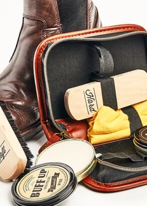 Ett skoputsningskit med borstar, putsduk och vax i ett skinnetui st&aring;r lutat mot en brun k&auml;nga.