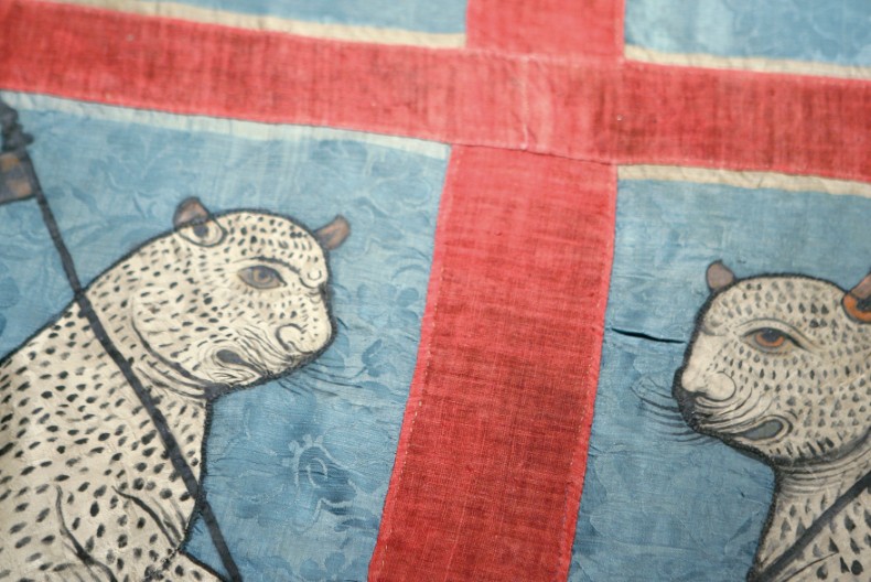 En närbild på en fana med rött kors mot blå botten och två kattdjur vända mot varandra