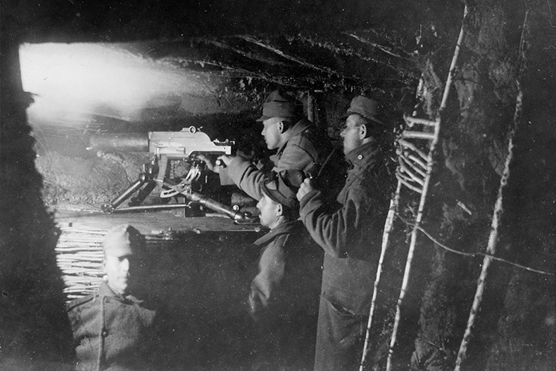 Fyra soldater i en skyttegrav, varav tre av dem står bakom en kulspruta och tittar bortåt.