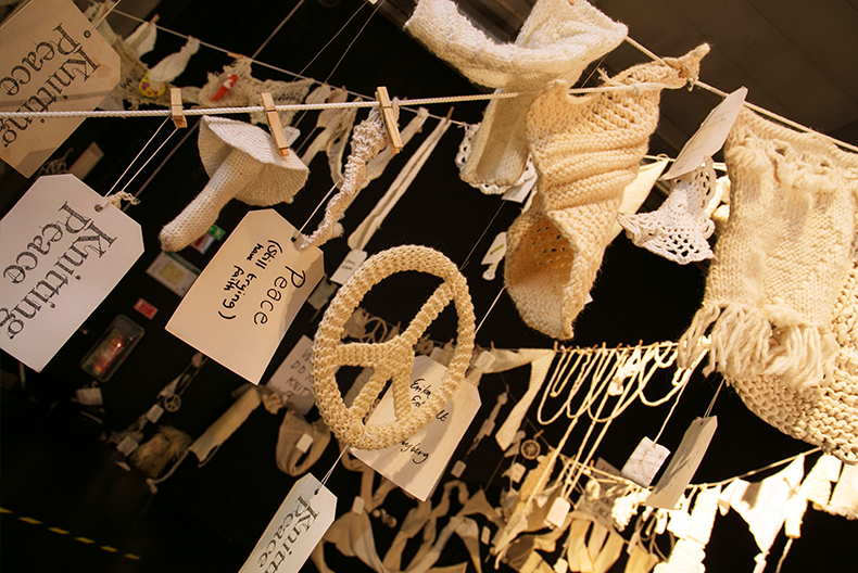 Tvättlinor hänger hit och dit med diverse föremål stickade i vitt garn. Här hänger även några papperslappar med bland annat texten "Knitting peace".