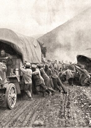 Svartvit bild av en stor folkmassa som hjälper två lastbilar upp på vägen igen. Vägen är lerig och den ena lastbilen verkar ha problem att komma upp ur ett dike.