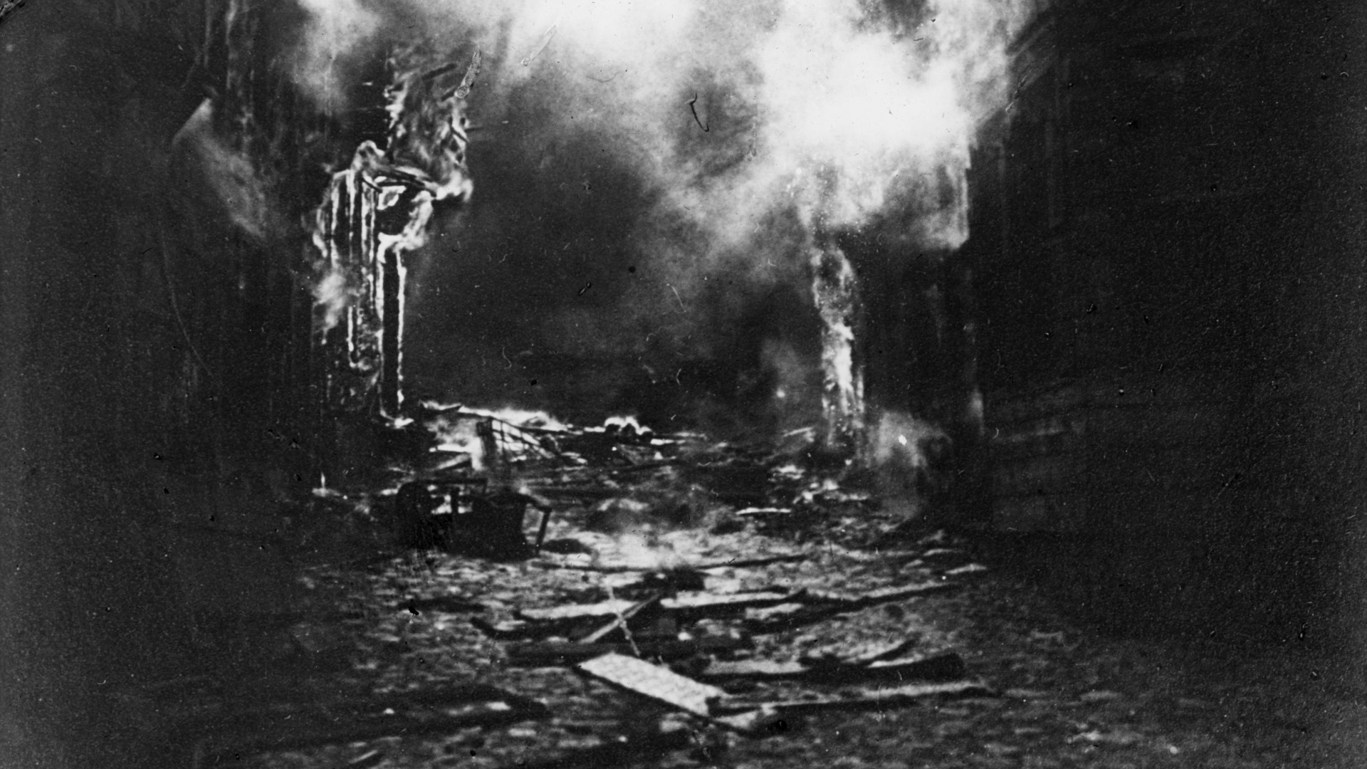 En svartvit bild av förstörelse. Rök stiger upp från vad som tidigare var byggnader.