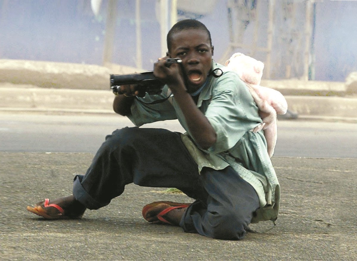 Ett barn med en ryggsäck i form av en nalle på ryggen riktar ett vapen mot den som tog bilden.