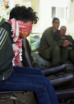 I förgrunden en bakbunden man på en stol och med förbundna ögon. I bakgrunden tre grönklädda män som ser ut att vänta på något.