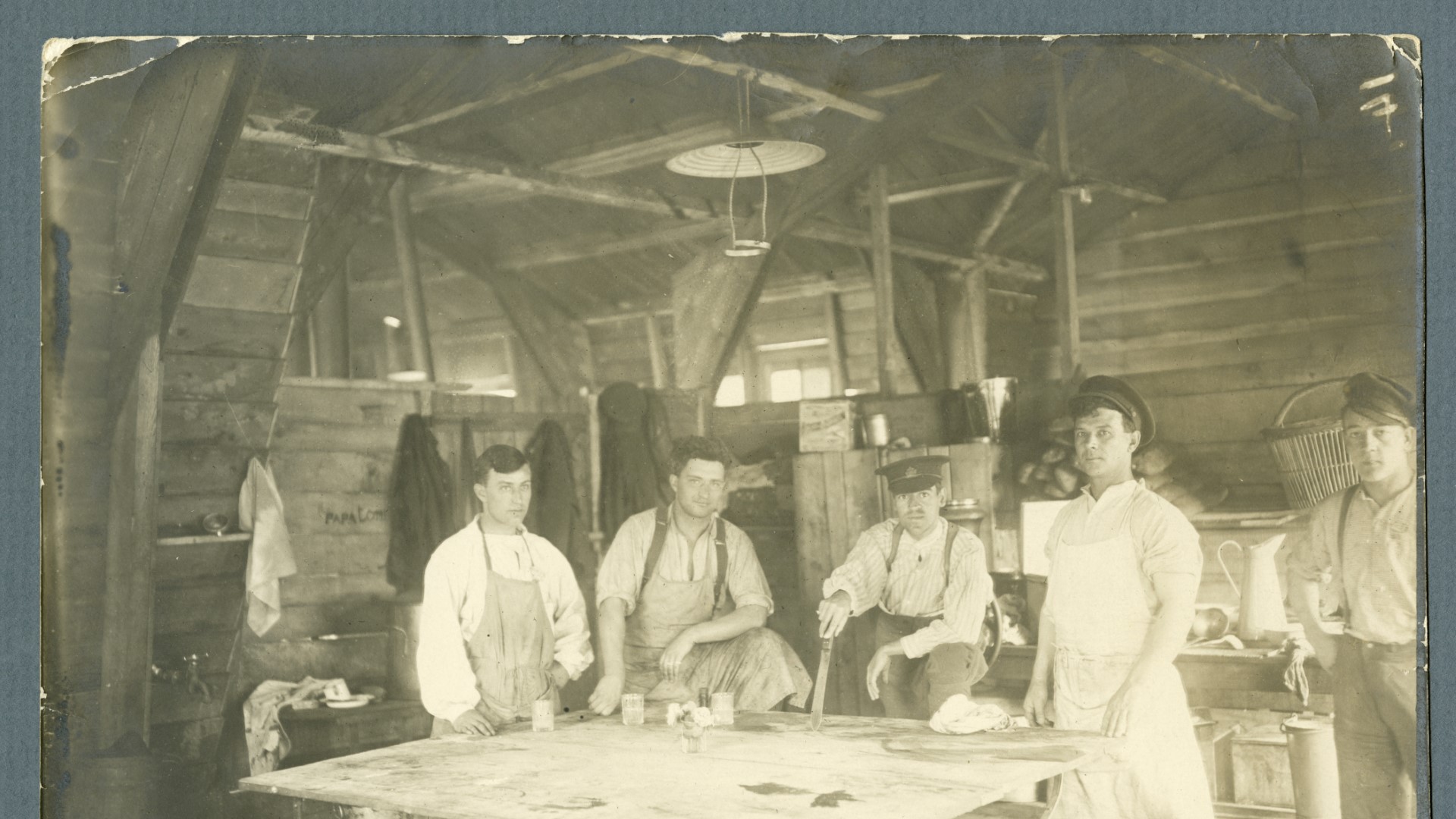 Fem vitklädda sjukvårdare iförda förkläden står vid ett vitt bord i en timrad byggnad.