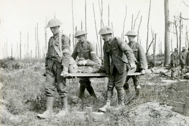 Fyra personer iförda uniform och hjälm bär på en person liggandes på en bår