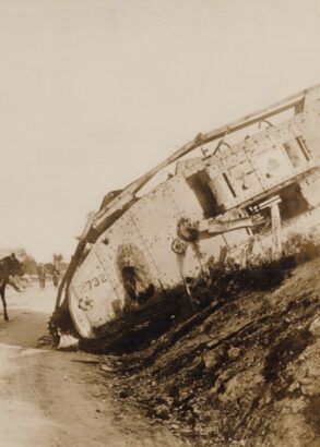 En stridsvagn har fastnat i terrängen, en häst med vagn med två passagerare passerar den på vägen bredvid.