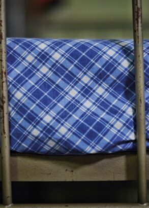 Del av en våningssäng i järn från lumpen, med blåvitrutiga, välsträckta lakan.