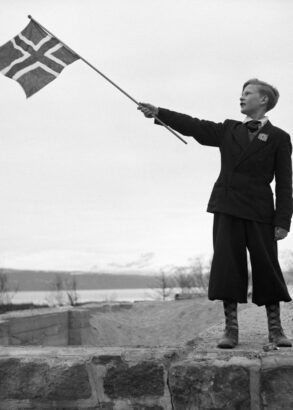 En person står på en stenmur och håller stolt upp Norges flagga.