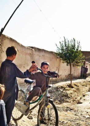Några barn leker längs en stenmur, en cyklar på en för stor cykel. Två soldater ser ut att patrullera genom området.