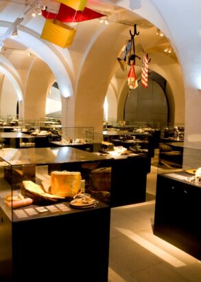 En utställningshall med valv i taket och flera glasmontrar fyllda med diverse föremål.