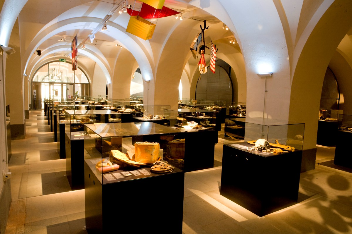 En utställningshall med valv i taket och flera glasmontrar fyllda med diverse föremål.