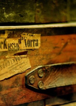 En närbild av en gammal koffert i trä med etiketter på, där handtaget i läder har gått av.