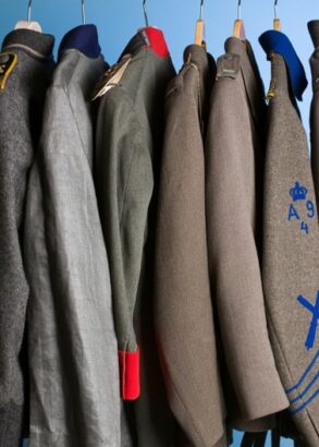 Nio uniformsjackor hänger på galgar på rad. Små detaljer skiljer dem åt såsom olika grå nyanser, ett rött slag, blå revärer.
