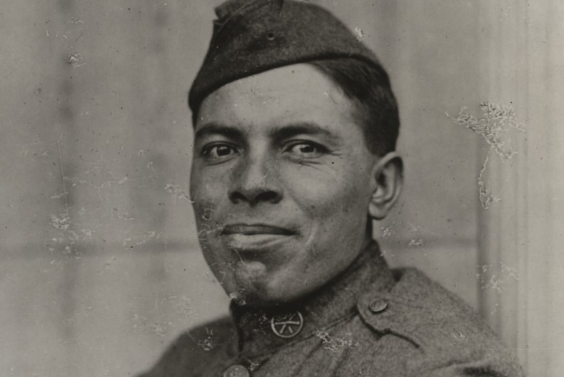 Porträtt av soldat iförd hatt och uniform. Grå bakgrund.