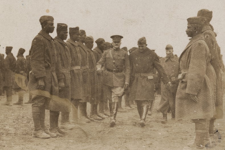 Uppställda soldater på led och i mitten går tre personer av högre rang fram.