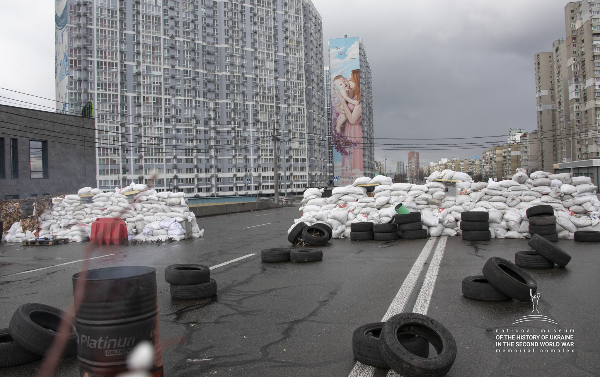 På en bilväg med höga byggnader längs sidorna har någon byggt vallar av sandsäckar och bildäck.