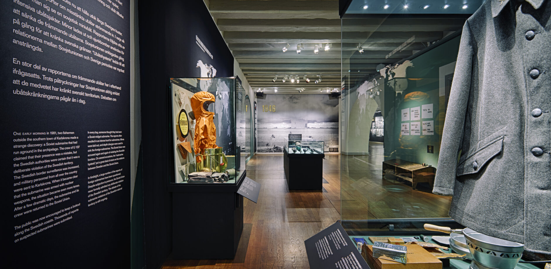  I förgrunden syns en mörk jacka med knappar och fickor som ingår i en utställning om kalla kriget. I bakgrunden syns montrar med föremål ur utställningen.
