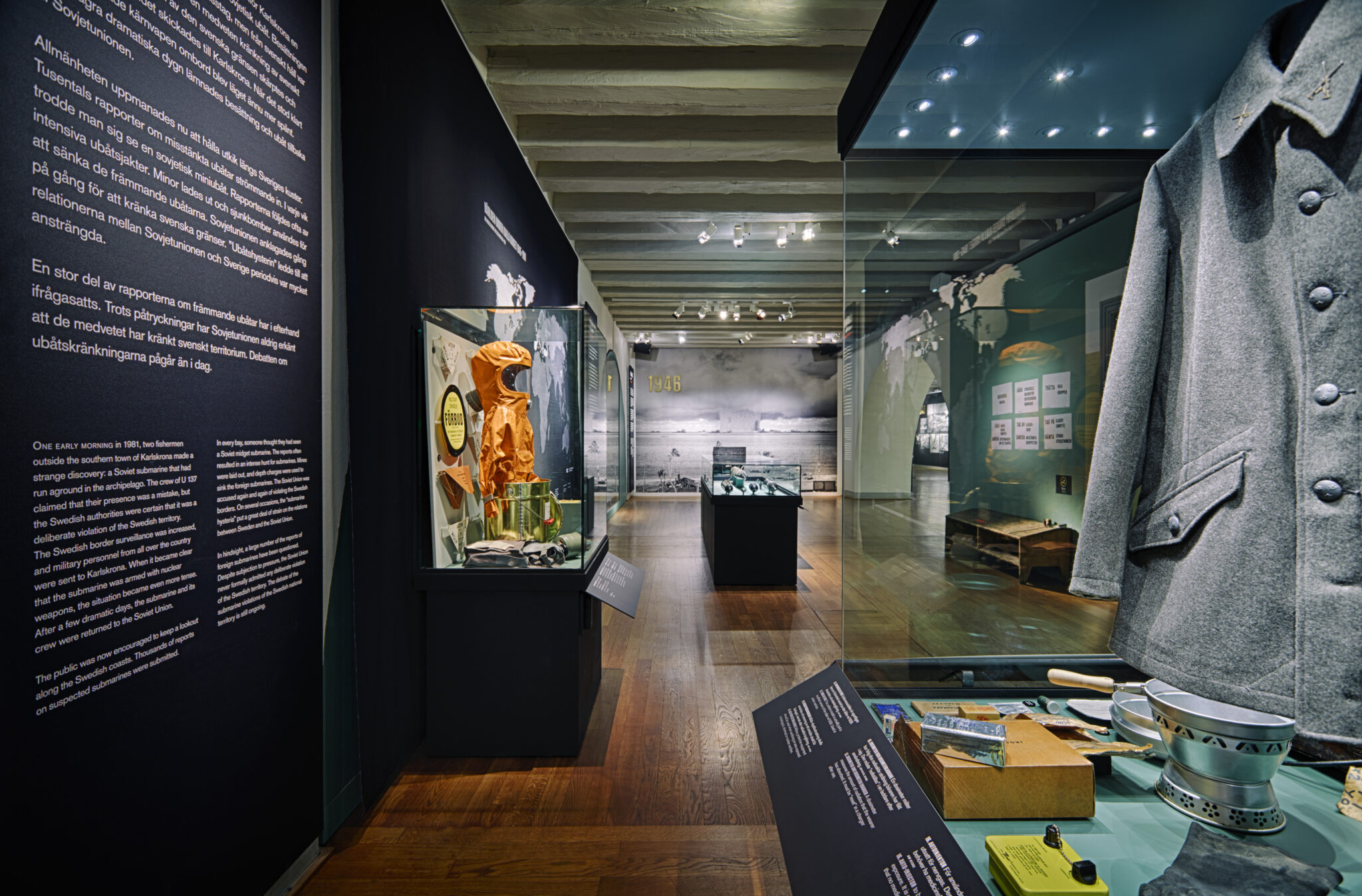 I förgrunden syns en mörk jacka med knappar och fickor som ingår i en utställning om kalla kriget. I bakgrunden syns montrar med föremål ur utställningen.