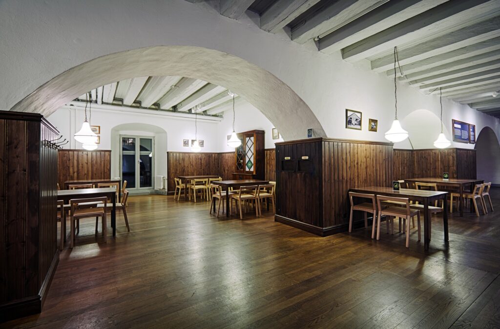 En lokal med valv och träpanel på väggarna med flera uppställda bord med stolar för den som vill sitta ner med sin matsäck.