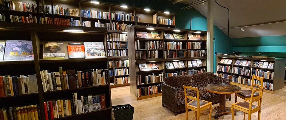 Vy från biblioteket, välfyllda bokhyllor på rad med plats att sitta ner i en soffa med bord och stolar