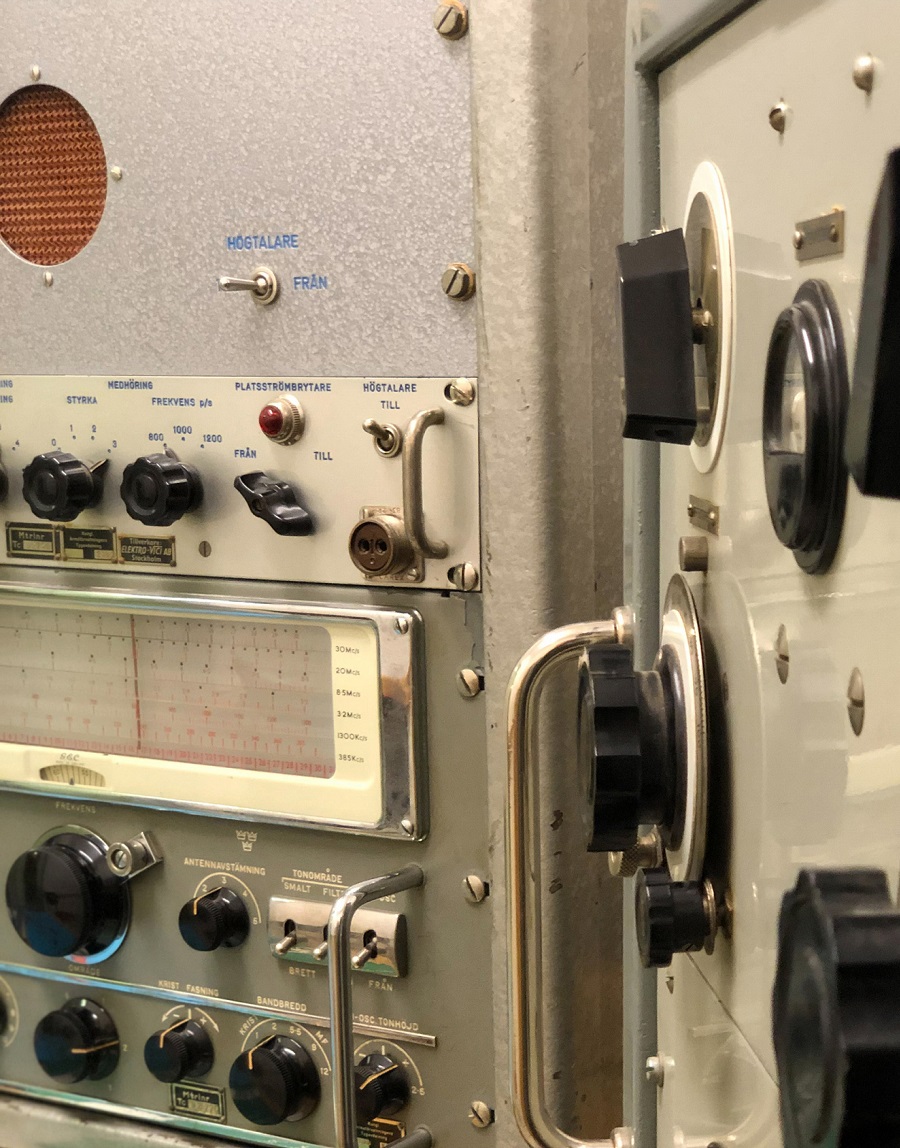 Närbild på en del av en kommunikationsutrustning i grått metallhölje med svarta rattar och reglage.